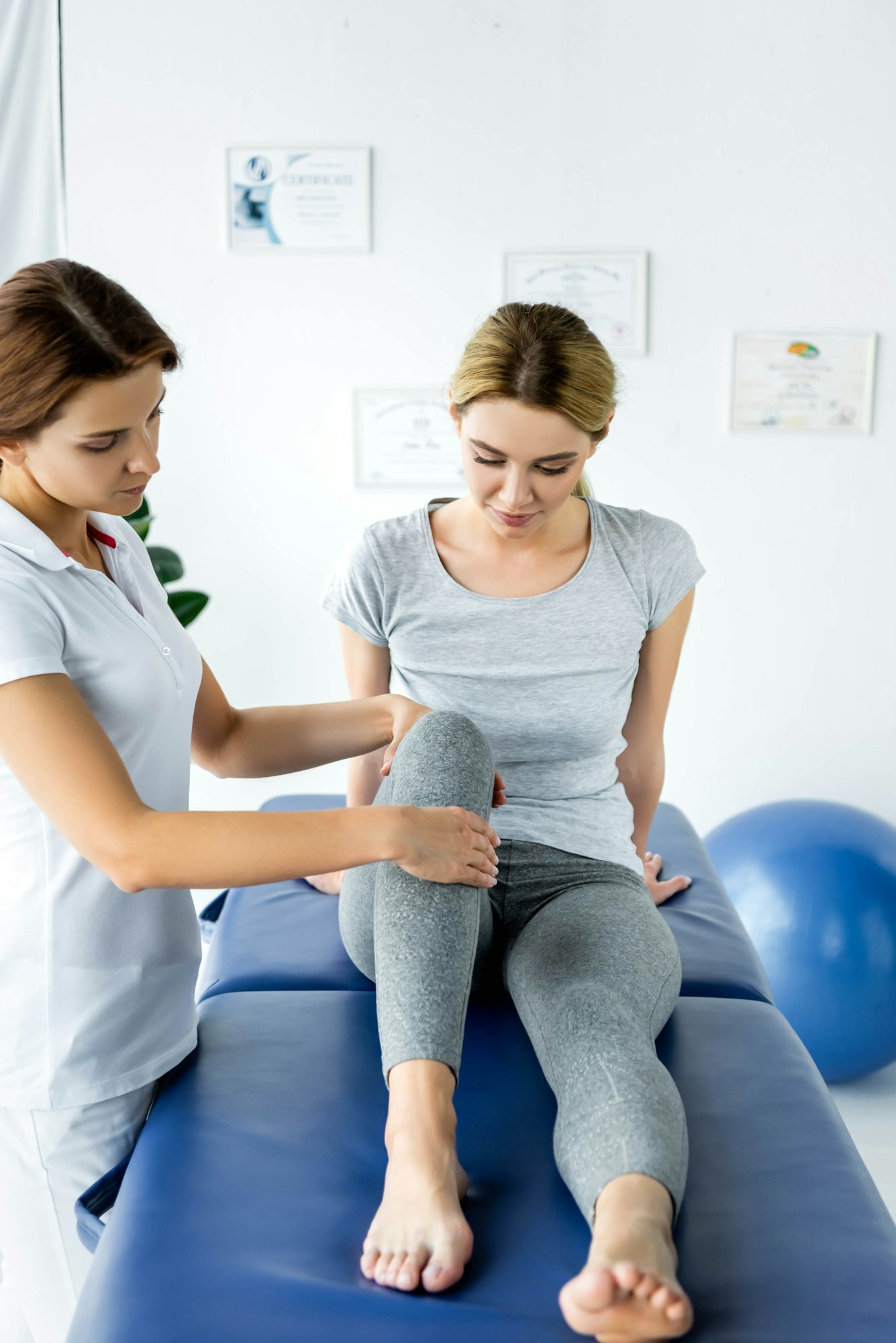 chiropractor touching leg of attractive patient in grey t-shirt chiropractor touching leg of attractive patient in grey t-shirt