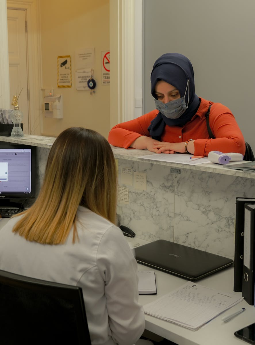 Patient visiting a chiropractic office reception, discussing appointment details with receptionist and filling out chiropractic patient records